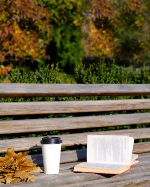 Paket kahve. Bankta bir kitap var. Yanında da espresso kahvesi olan bir kağıt bardak. Sonbahar yaprakları. Ahşap arka plan. Sonbahar bileşimi.