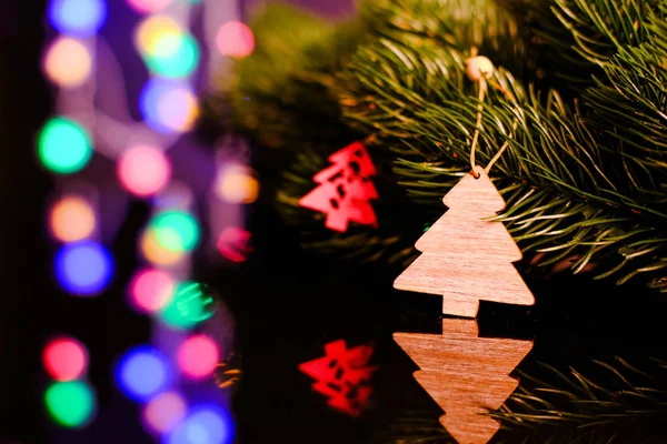 Weihnachtsspielzeug aus Holz hängt an einem Fichtenzweig. Karte. magischer heller Hintergrund. Reflexion in schwarzem Glas. — Stockfoto