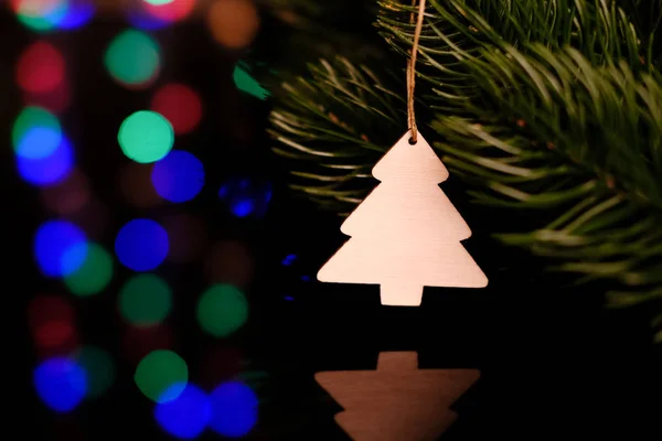 Weihnachtsspielzeug aus Holz, das an einem Fichtenzweig hängt. Karte. magischer heller Hintergrund. Reflexion in schwarzem Glas. — Stockfoto