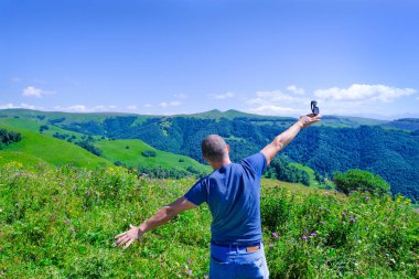 Erkek turist ellerini kaldırıyor ve doğa, orman ve dağların muhteşem manzarasının tadını çıkarıyor. Dağlık arazi