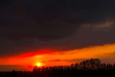 Güneşli ve bulutlu kırmızı günbatımı gökyüzü. Güneşin parlak diski. Güzel ve renkli gün batımı gökyüzü.