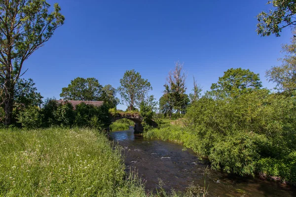 강, 오래된 다리, 나무와 푸른 하늘과 화창한 여름 시골 풍경. — 스톡 사진