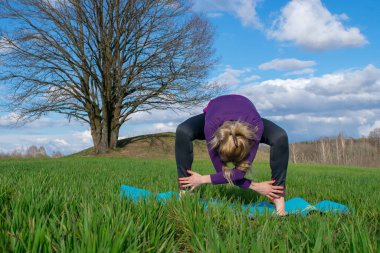 Orta yaşlı sarışın bir kadın doğada yoga yapıyor. Sağlıklı bir yaşam tarzı. Vücut konsantrasyonu. Kişisel bakım kavramı..