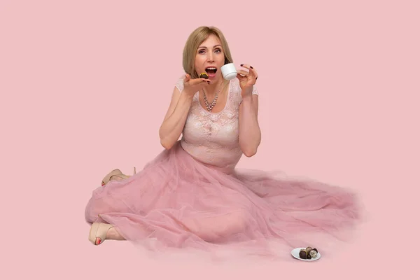 Beautiful Woman With Cup of Tea or Coffee. Studio portrait of a dreamy blonde woman wearing a pink airy skirt, holding a cup of coffee and chocolate in her hands, drinking fresh tasty drink