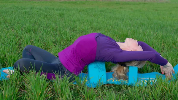 A middle-aged blonde woman in a tracksuit practices yoga outdoors. Healthy lifestyle and Slow life alone with nature. Taking care of yourself to stay healthy.