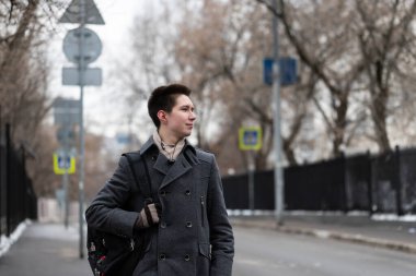 Ceket giymiş genç ve özgür bir moda adamı evden sokağa sırt çantasıyla gezmeye ya da ders çalışmaya gider.