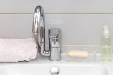 Modern el yıkama leğeni. Sağlam masa üstü yüzeyi ve gri fayans duvarı. Lavabodaki musluğun yanında harcanabilir sabun.