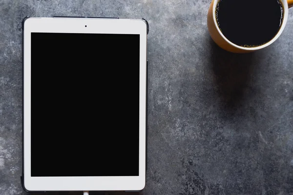 Coffee break. Top view yellow cup of coffee with tablet on a table background