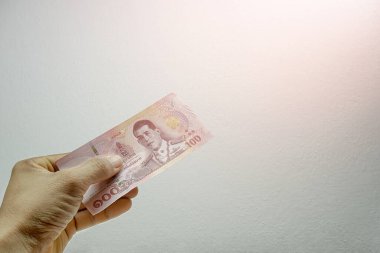 Bir adamın eli beyaz arka planda 100 banknot tutuyor. Tayland baht para birimi banknotu kavramı