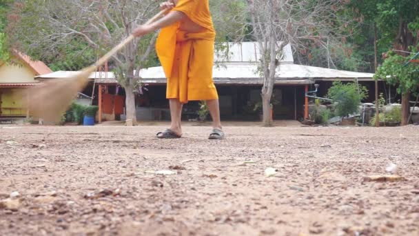 Ένας νεαρός Βουδιστής μοναχός στην Ταϊλάνδη σαρώνει το έδαφος του ναού αφού χειροτονήθηκε σύμφωνα με τα ταϊλανδικά έθιμα για την αντικατάσταση των πατέρων και των μητέρων. — Αρχείο Βίντεο