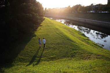 Genç çift gün batımında nehir kıyısında yürüyor.