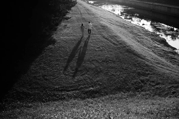 日落时分,年轻夫妇正沿着河岸散步. — 图库照片