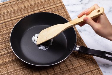 Kadın eli hindistan cevizi yağını kızartma tavasında spatulayla karıştırıyor.