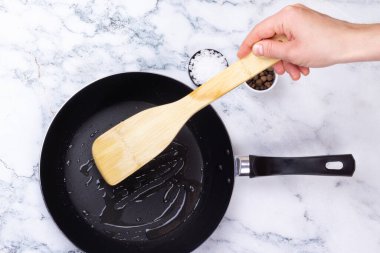 Kadın eli hindistan cevizi yağını kızartma tavasında spatulayla karıştırıyor.