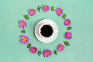 Beyaz fincanda Americano kahvesi ve pembe kasımpatı çiçekleri, yeşil yapraklı yeşil nane arkaplanı. 