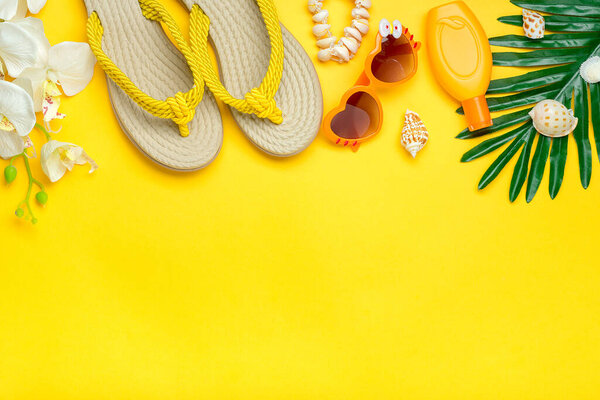 Swimming accessories - orchid flowers, sunblock, heart - shaped glasses, flip flop, palm, shells isolated on yellow background Flat lay Top view