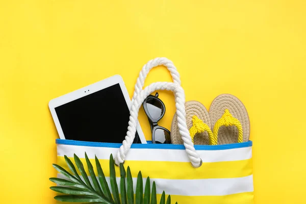 Swimming accessories - trendy beach bag with stripes, black glasses, white tablet, palm leaf, yellow flip flop on yellow background Flat lay Top view Summer, travel, vacation concept Holiday card