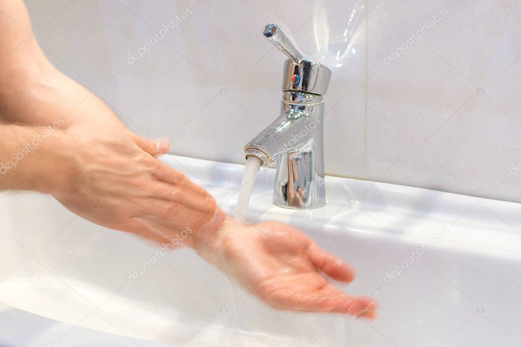 closeup of young caucasian man washing his hands with soap in the sink of bathroom Personal hygiene, protection against viruses and bacteria concept.