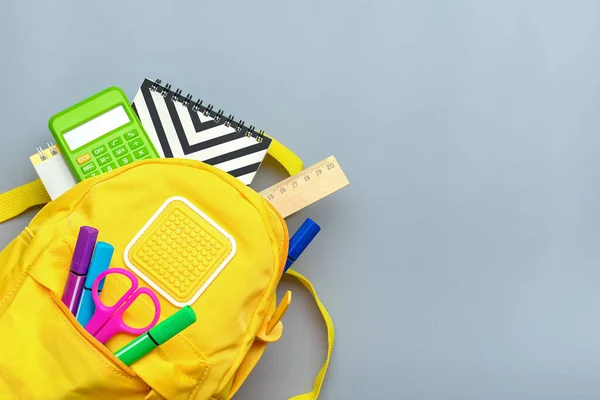Back to school, education concept. Yellow backpack with school supplies - notebook, pens, ruler, calculator, scissors isolated on gray background. Top view. Copy space Flat lay composition Banner.