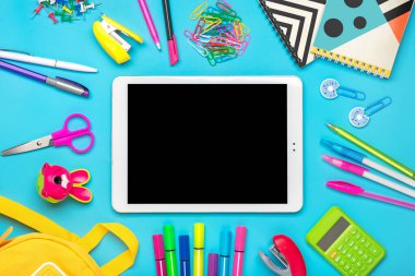 Okula dönmek, eğitim kavramı. Okul gereçleri içeren sarı sırt çantası Not defteri, kalemler, cetvel, hesap makinesi, makas, tablet mavi arkaplan üzerinde izole edilmiş Üst görünüm Üst Alan Kopyalama kompozisyonu.