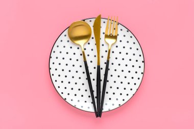 Siyah bezelyeli, çatallı, bıçaklı boş beyaz tabak, modaya uygun pembe arka planda kaşık kahvaltı, öğle yemeği ya da akşam yemeği için düz tabaklar seriliyor..