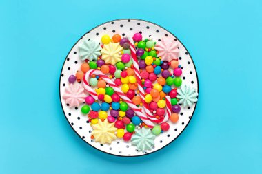 Renkli şekerlerin karışımı - beyaz yuvarlak tabak ile siyah bezelye, lolipop, krema, çikolata, mavi arka planda serpiştirilmiş şeker Üst manzara tatil kartı kartı mutlu yıllar, Sevgililer Günü konsepti