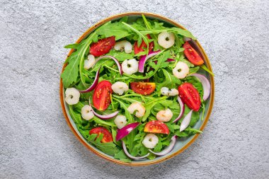 Akdeniz diyet menüsü konsepti. Taze sebzelerden oluşan sağlıklı bir salata. Domates, roka, mor soğan, karides, soya sosu ve gri beton masa üzerinde susam tohumları..