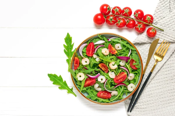 Mediterranean diet menu concept Healthy salad of fresh vegetables - tomatoes, arugula, purple onions, shrimps, soy sauce and sesame seeds in plate on white wooden table Vegan food Flat lay Top view.
