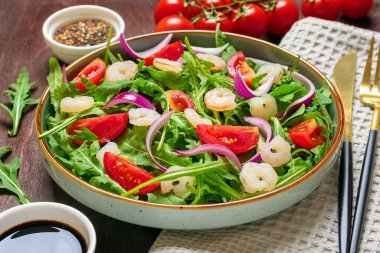 Akdeniz diyet menüsü konsepti taze sebzelerden oluşan sağlıklı salata - domates, roka, tabakta mor soğan, susam tohumu, soya sosu, bıçak, çatal, peçete, ahşap masa vejetaryeni üst görünüm.