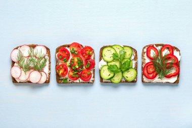 Kahvaltı için çeşitli sandviçler - bir dilim kepekli ekmek, biber, krem peynir, salatalık, turp, kiraz domatesli, dereotla süslenmiş, mavi masanın üstünde yeşil soğan.