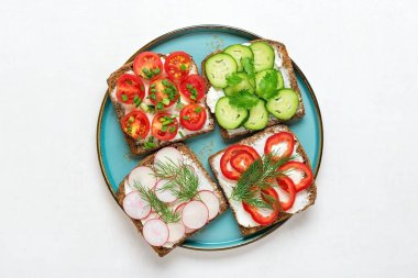 Kahvaltı için çeşitli sandviçler - bir dilim kepekli ekmek, biber, krem peynir, salatalık, turp, kiraz domatesli, dereotla süslenmiş, beyaz masa üzerinde yeşil soğan.