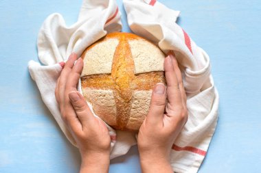 Kadın elleri taze pişmiş mayalı ekmeği fırından peçeteyle mavi ahşap masanın üstünde düz bir şekilde ev yapımı hamur işi yatıyordu..