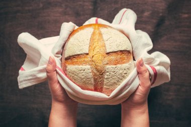 Kadın elleri taze pişmiş mayalı ekmeği fırından peçeteyle mavi ahşap masanın üstünde düz bir şekilde ev yapımı hamur işi yatıyordu.