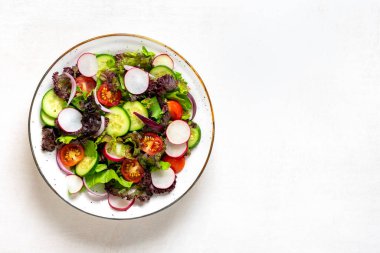 Sağlıklı sebze salatası kiraz domatesleri, salatalık dilimleri, yeşil ve mor marul yaprakları, soğan ve zeytinyağı tabakta beyaz ahşap masa üstünde düz tabakta Diyet, Akdeniz menüsü vegan yemeği