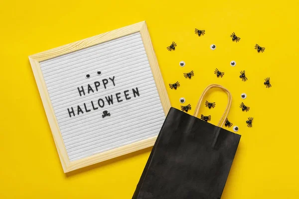 Felt board with text and black package, crawling spiders on yellow background Top view Flat lay Happy Halloween creative concept Holiday card — Stock Photo, Image