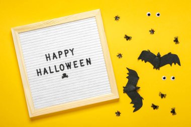 Keçeli tahta, metin, tırnak içinde, siyah yarasa, sarı arka planda örümcekler düz düz uzanan Mutlu Cadılar Bayramı yaratıcı konsepti Tatil kartı afişi