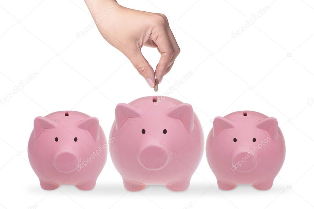 Hand putting coin into piggy bank. Three ceramic piggy banks on a white background
