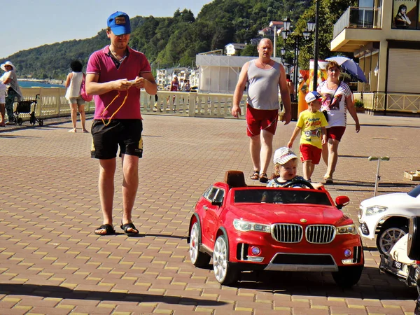 Un niño rubio monta una máquina de escribir roja a lo largo del terraplén del Mar Negro — Foto de Stock