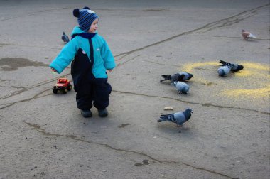 Mavi tulumlu bebek güvercinleri ekmekle besliyor