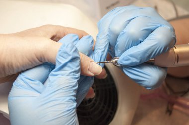 Kadın eli - mavi eldivenli usta müşteriye donanım manikürü yapıyor.