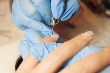 Kadın eli - mavi eldivenli usta müşteriye donanım manikürü yapıyor.