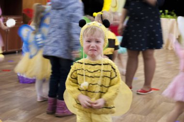 Üç yaşında bir çocuk, mavi gözlü üzgün sarışın bir çocuk, arı kostümü giymiş.