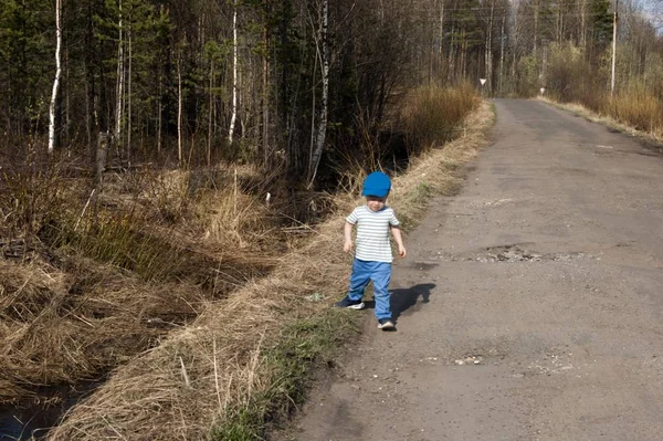 Ранняя весна, маленький трехлетний мальчик в синих штанах, один на проселочной дороге — стоковое фото