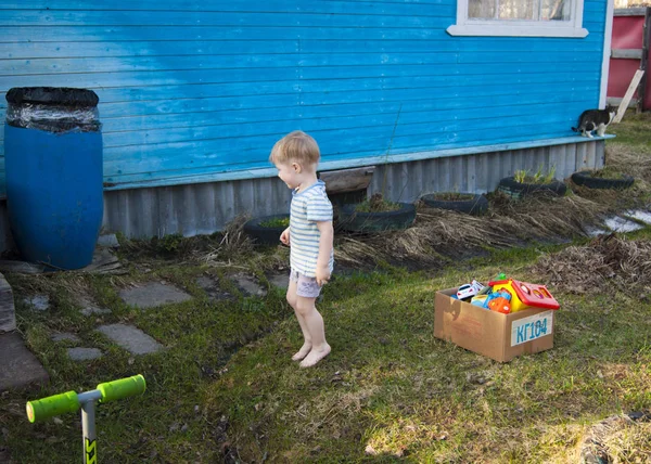 Ранней весной деревня, трехлетний блондин в футболке и шортах гуляет по двору босиком по молодой траве . — стоковое фото