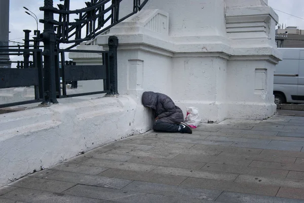 Eine obdachlose Frau schläft am helllichten Tag direkt auf der Straße, ihre Sachen liegen in der Nähe in einer Tüte. Redaktionsfoto — Stockfoto