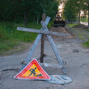 Yol onarım çalışmaları - sarı bir traktör tamir edecek kaldırım, üzerinde duruyor. Ön planda bir tanksavar kirpi ve onarım çalışmaları hakkında bir uyarı işareti