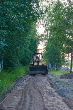 Yol onarım çalışmaları - sarı bir traktör tamir edecek kaldırım, üzerinde duruyor. Ön planda bir kum yolu var