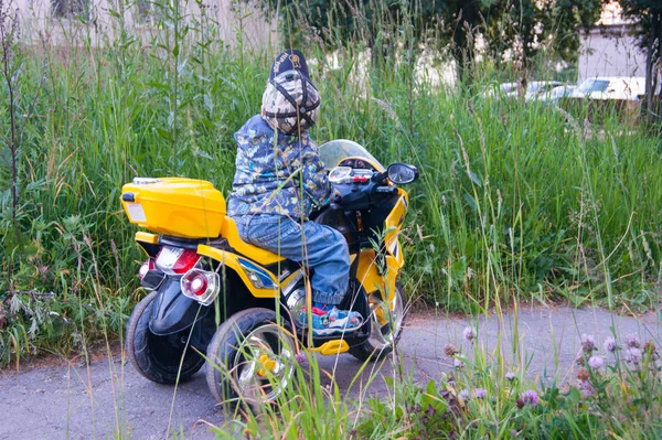Un bébé de trois ans coiffé d'une casquette et d'une veste roule sur sa moto électrique jaune pour enfants. Voiture électrique. Enfance, divertissement, activité, bonheur, émotions — Photo