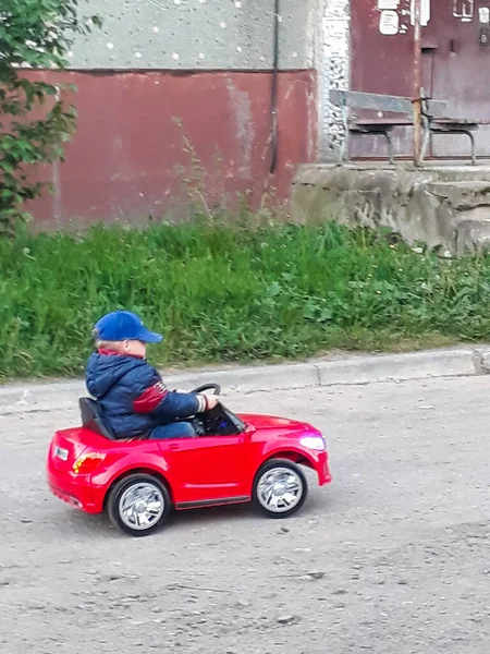 Menino branco de três anos em um carro elétrico vermelho das crianças monta pelas ruas da cidade — Fotografia de Stock