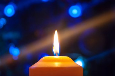 Koyu bir arka planda yanan turuncu bir mum. Mavi ışıklarla. Yeni yıl arifesinde gizemli, gizemli bir aşk havası. Yatay fotoğraf, kenar, odaklan veya ayrıl